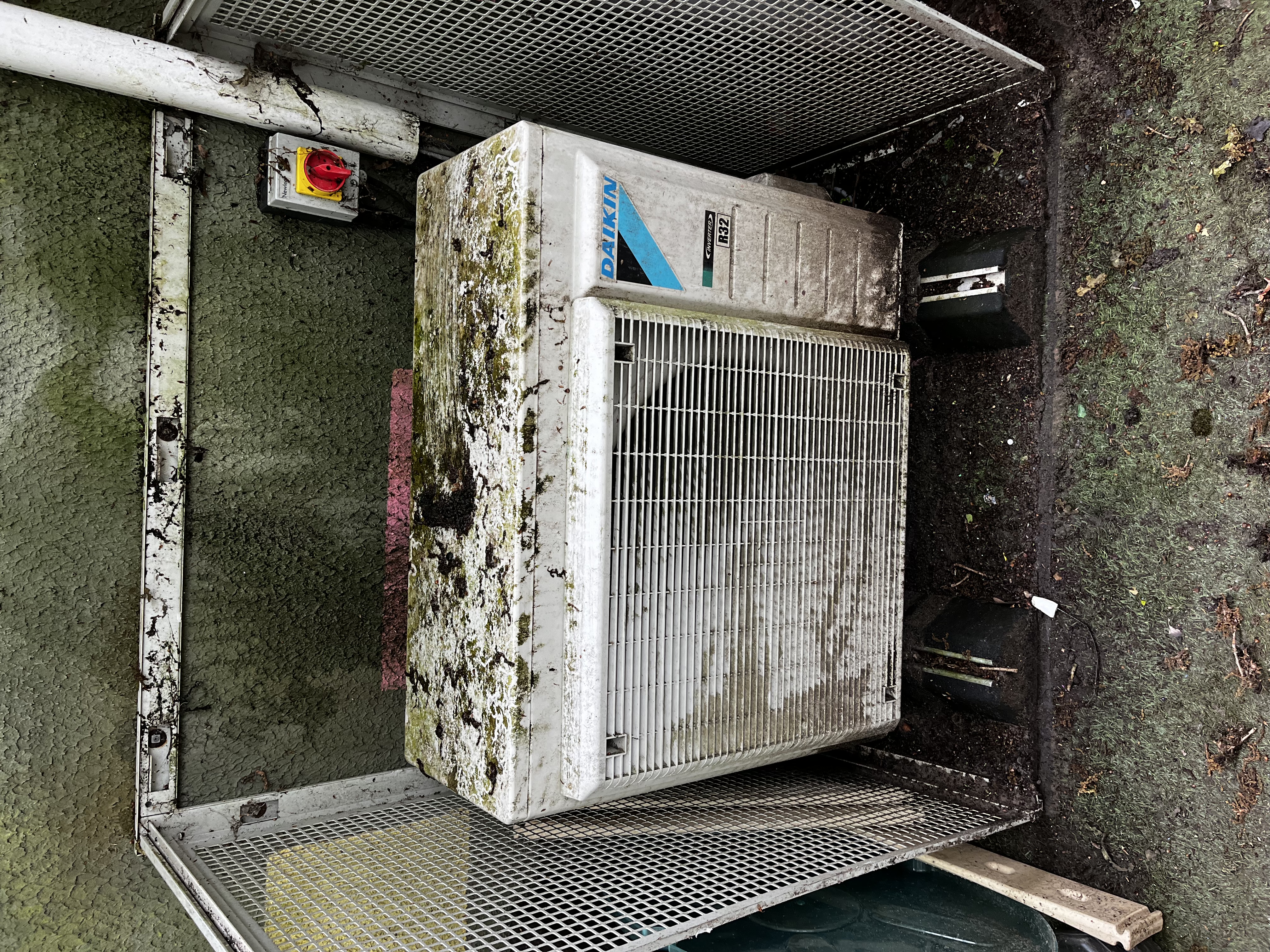 Outdoor Daikin air conditioning unit before cleaning, with dirt and moss on its casing